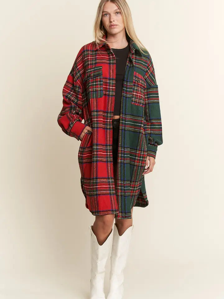 Model wearing a longline holiday plaid jacket with contrasting red and green panels and chest pockets.