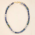 Mixed-bead necklace in blue, lavender, pale neutral, and iridescent green tones with a gold-tone clasp and extender