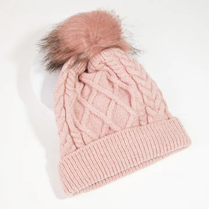 Blush pink cable knit beanie with a ribbed folded cuff and fluffy pink pom with darker accents
