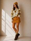 Model wearing a cream-colored sweater with yellow sunflowers and green leafy accents, styled with a mustard skirt.