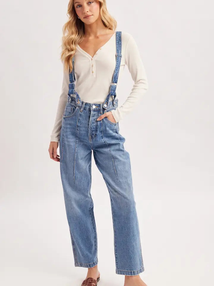 Blue denim suspender jeans with wide legs and front seam detailing, styled with a cream long-sleeve top.