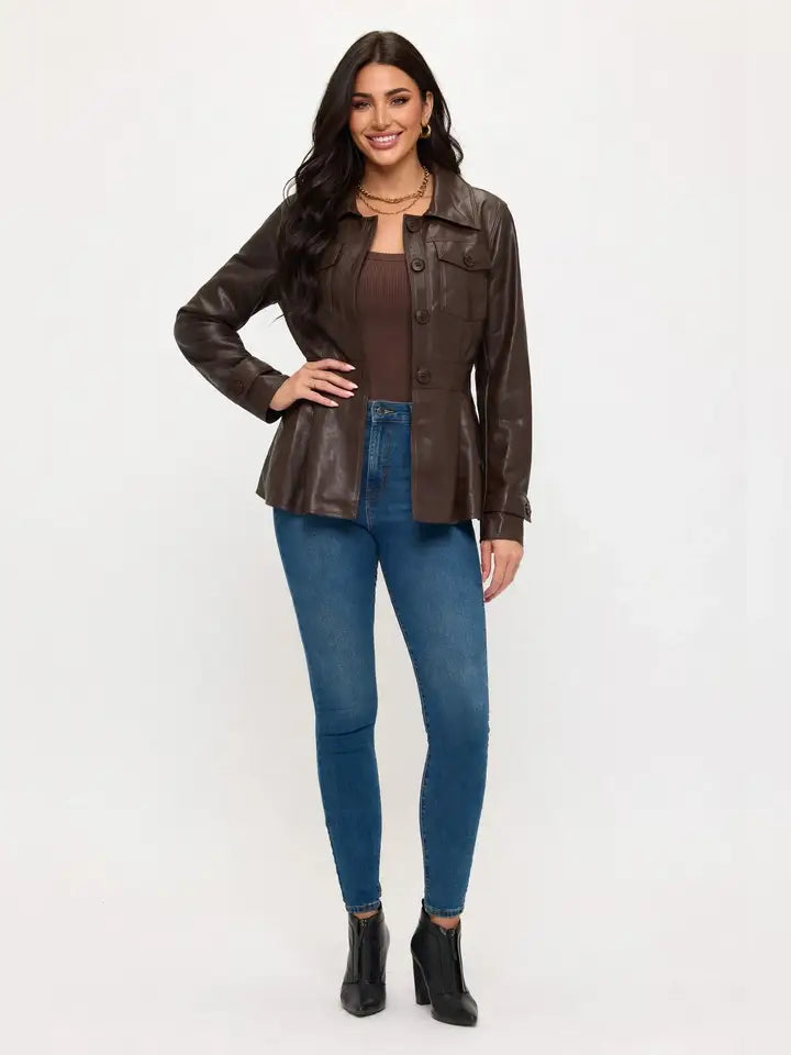 Brown utility faux leather jacket with a pointed collar, front buttons, and chest flap pockets, styled with blue jeans.