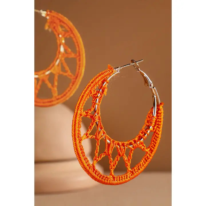 Orange crochet knit hoop earrings on warm neutral background
