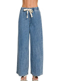 Model wearing medium wash wide leg drawstring jeans with elastic waist and cream drawstring tie, styled with white sandals