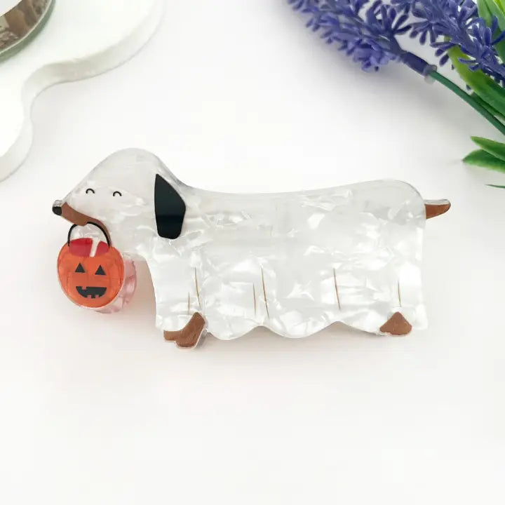 Ghost Dog Claw Clip featuring a pearlescent white dachshund in a ghost costume holding an orange jack-o-lantern pumpkin