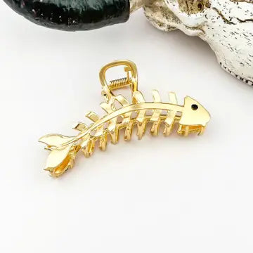 Gold Fishbone Claw Clip sculpted as a full fish skeleton in warm gleaming gold with detailed rib bones, tail fin, and black eye