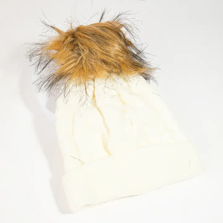 Ivory cable knit beanie with a folded cuff and fluffy brown pom on top