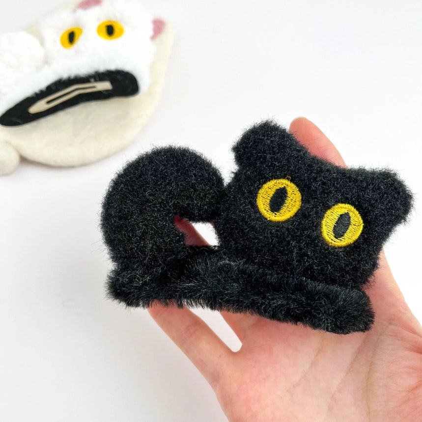 Plush White Cat Alligator Clip held in hand showing size, with black cat clip in background