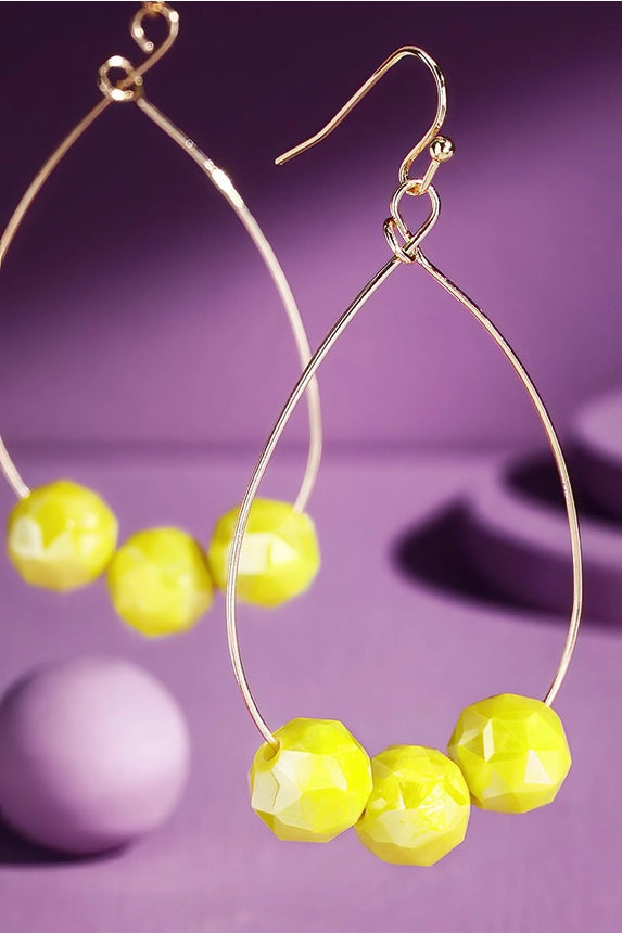 Neon yellow crystal ball teardrop hoop earrings on purple background