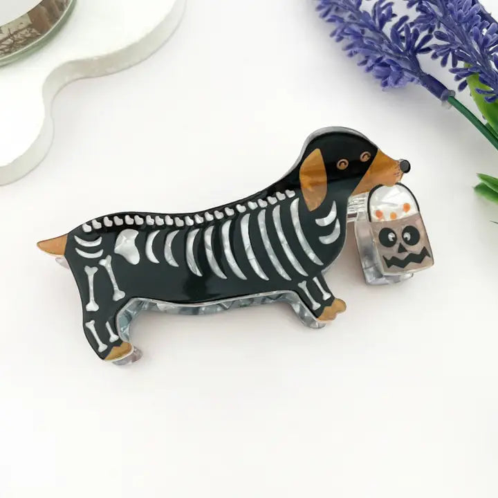 Skeleton Dog Claw Clip featuring a dachshund in a skeleton costume holding a ghost jack-o-lantern trick-or-treat bucket